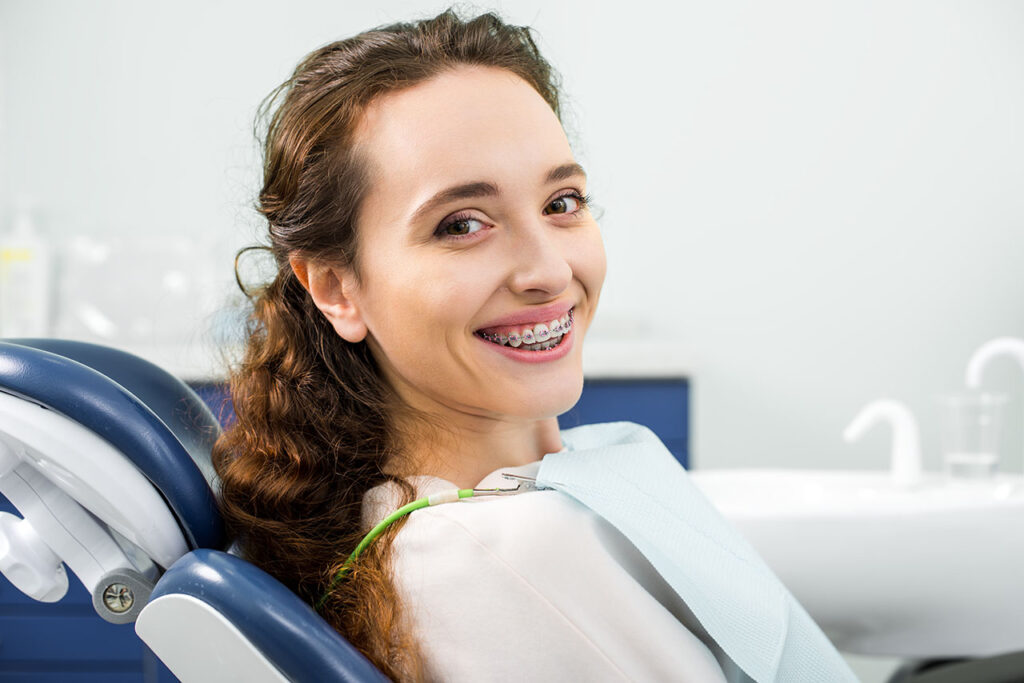 Diş kliniğinde muayene sırasında diş telleri takmış mutlu bir kadın gülümsüyor.